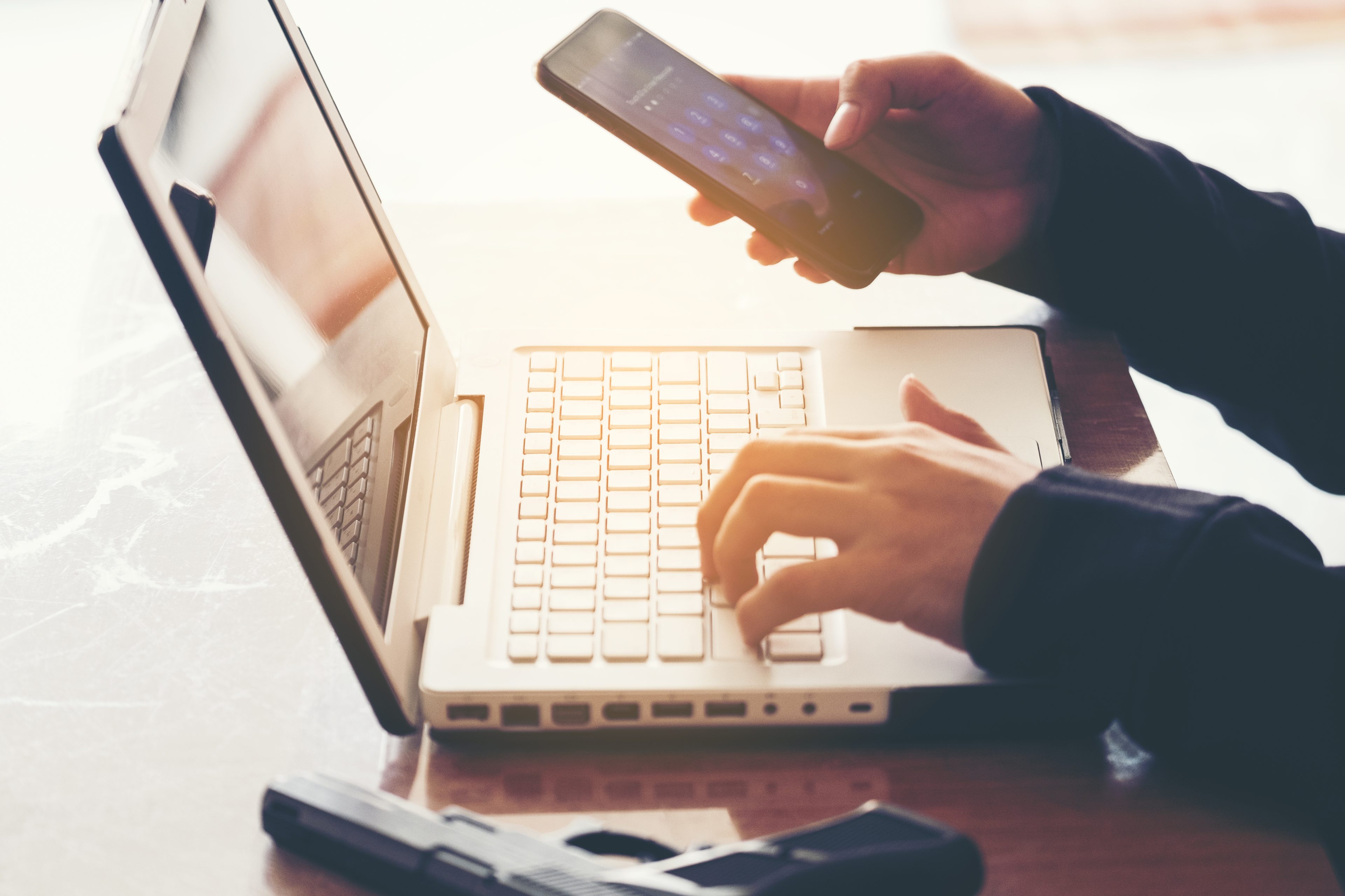 Businesswomen typing at computer with cellphone in hand
